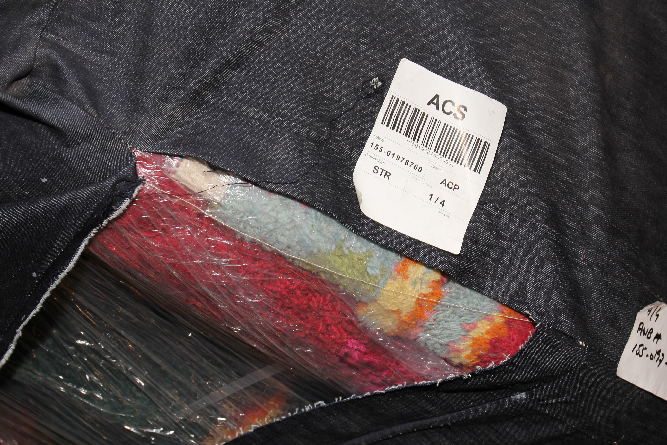 Eine dunkle Tasche aus der ein bunter in Plastik verpackter Teppich rausblitzt