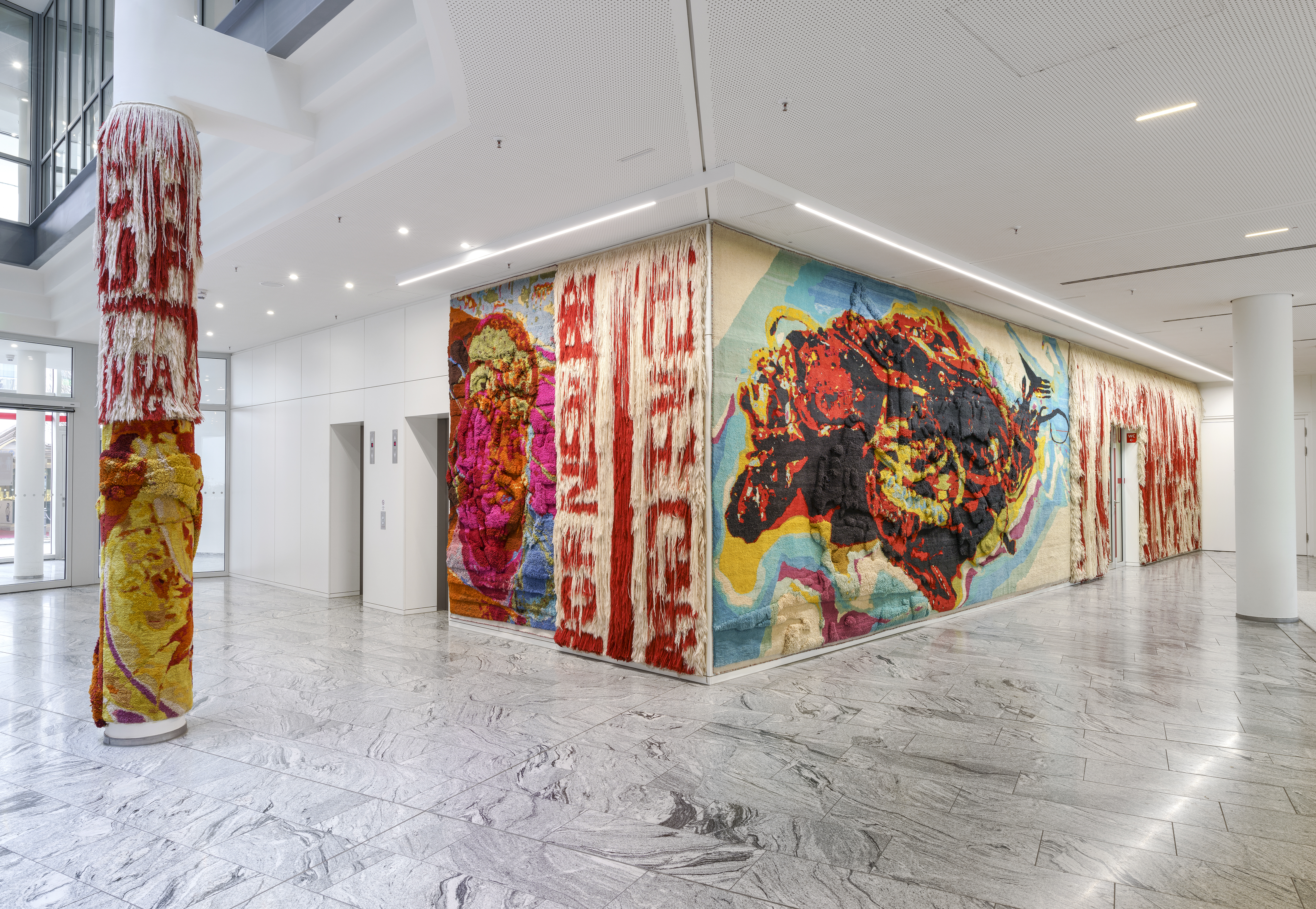 Eckansicht. An der Wand aufgehängte, bunte Teppiche in den Innenräumen der Kreissparkasse Esslingen-Nürtingen